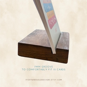 May include: A dark brown wooden card holder with a 7mm groove designed to comfortably fit 15 cards. The holder supports a card with colorful illustrations. The Etsy shop name is visible at the bottom.