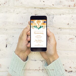 May include: A smartphone displaying a housewarming invitation. The invitation features an ornate gold and teal design with the words "Housewarming" and event details. The phone is held by two hands against a white brick wall.