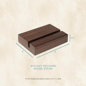 May include: A rectangular walnut wood stand with a slot, measuring 4 inches long, 3 inches wide, and .75 inches high. The stand is polished and features the text "WALNUT POLISHED WOOD STAND".