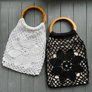 May include: Two crochet handbags with circular handles. One bag is white with a bamboo-style handle and a floral pattern. The other bag is black with a smooth wooden handle and a matching floral crochet design. Both bags feature an inner lining.