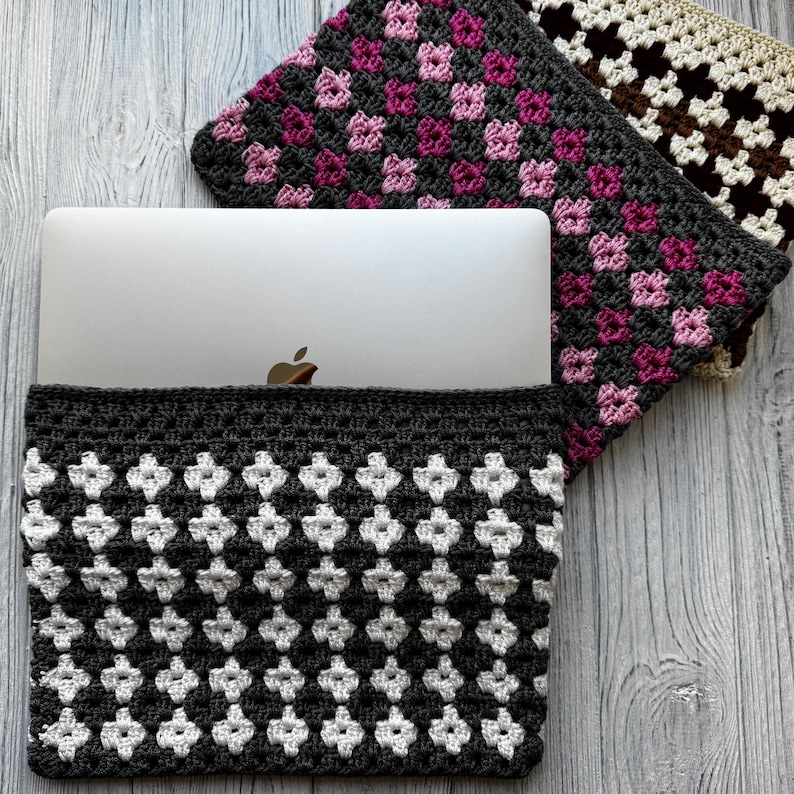 May include: A gray and white crocheted laptop sleeve with a geometric pattern, holding a silver laptop. Two additional crocheted cases in pink and brown floral patterns are visible.