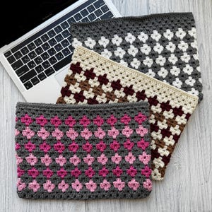 May include: Three crocheted laptop sleeves in varying colors and patterns. The top sleeve is gray with white diamond shapes. The middle sleeve is beige with brown and burgundy diamonds. The bottom sleeve is gray with pink diamond shapes. A laptop is partially visible.