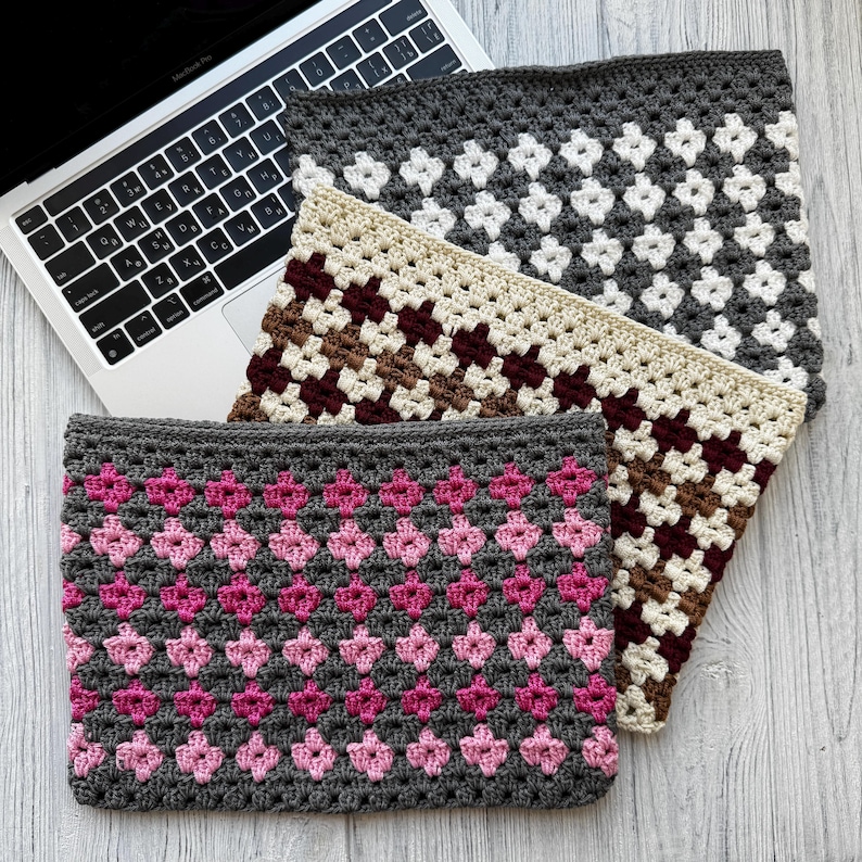 May include: Three crocheted laptop sleeves in varying colors and patterns. The top sleeve is gray with white diamond shapes. The middle sleeve is beige with brown and burgundy diamonds. The bottom sleeve is gray with pink diamond shapes. A laptop is partially visible.