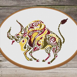 May include: A cross-stitch embroidery design of a stylized bull with intricate patterns in shades of yellow, red, and brown. The bull is depicted in a standing position with its head turned to the side.