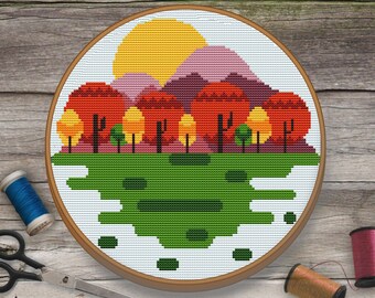 Peut inclure: Une broderie au point de croix dans un cercle en bois. Le motif représente un soleil jaune, des montagnes violettes et des arbres rouges, oranges et verts. La scène est sur fond blanc. Des fournitures de couture, dont du fil et des ciseaux, sont visibles.