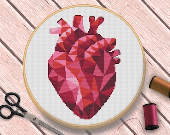 Puede incluir: Un patrón de punto de cruz de corazón geométrico en tonos de rosa y rojo, enmarcado en un aro de madera. El aro está sobre una superficie de madera.