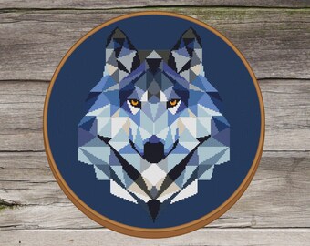 Peut inclure: Un motif de tête de loup géométrique dans des tons de bleu, violet et blanc, avec un œil jaune, sur un fond bleu foncé. Le motif est encadré dans un cerceau en bois.