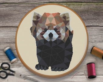 May include: A geometric cross-stitch pattern of a red panda in a hoop. The red panda is brown, black, and white with a geometric design. The hoop is on a wooden surface.