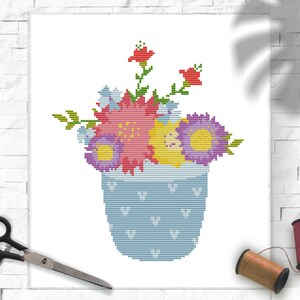 Puede incluir: Un patrón de punto de cruz de un jarrón azul con un arreglo floral de flores rojas, amarillas y moradas.