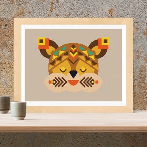 May include: A framed cross-stitch pattern of a stylized animal face with geometric patterns in shades of brown, orange, yellow, and blue. The animal has closed eyes and a small, smiling mouth.