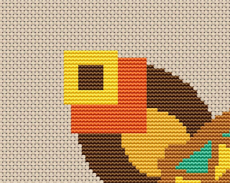 May include: Cross-stitch pattern featuring a geometric design with brown, yellow, orange, and teal squares. The pattern is stitched on a beige fabric.