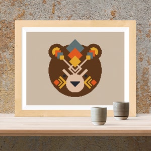 Peut inclure: Un motif de point de croix encadr&eacute; repr&eacute;sentant un ours brun avec un motif g&eacute;om&eacute;trique sur la t&ecirc;te. Le motif est compos&eacute; de couleurs jaunes, orange, rouge, bleu et blanc.