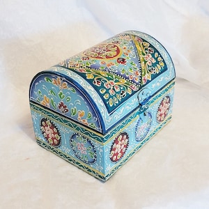May include: A blue wooden box with a hinged lid decorated with colorful floral patterns. The box has a traditional design and is perfect for storing small items.