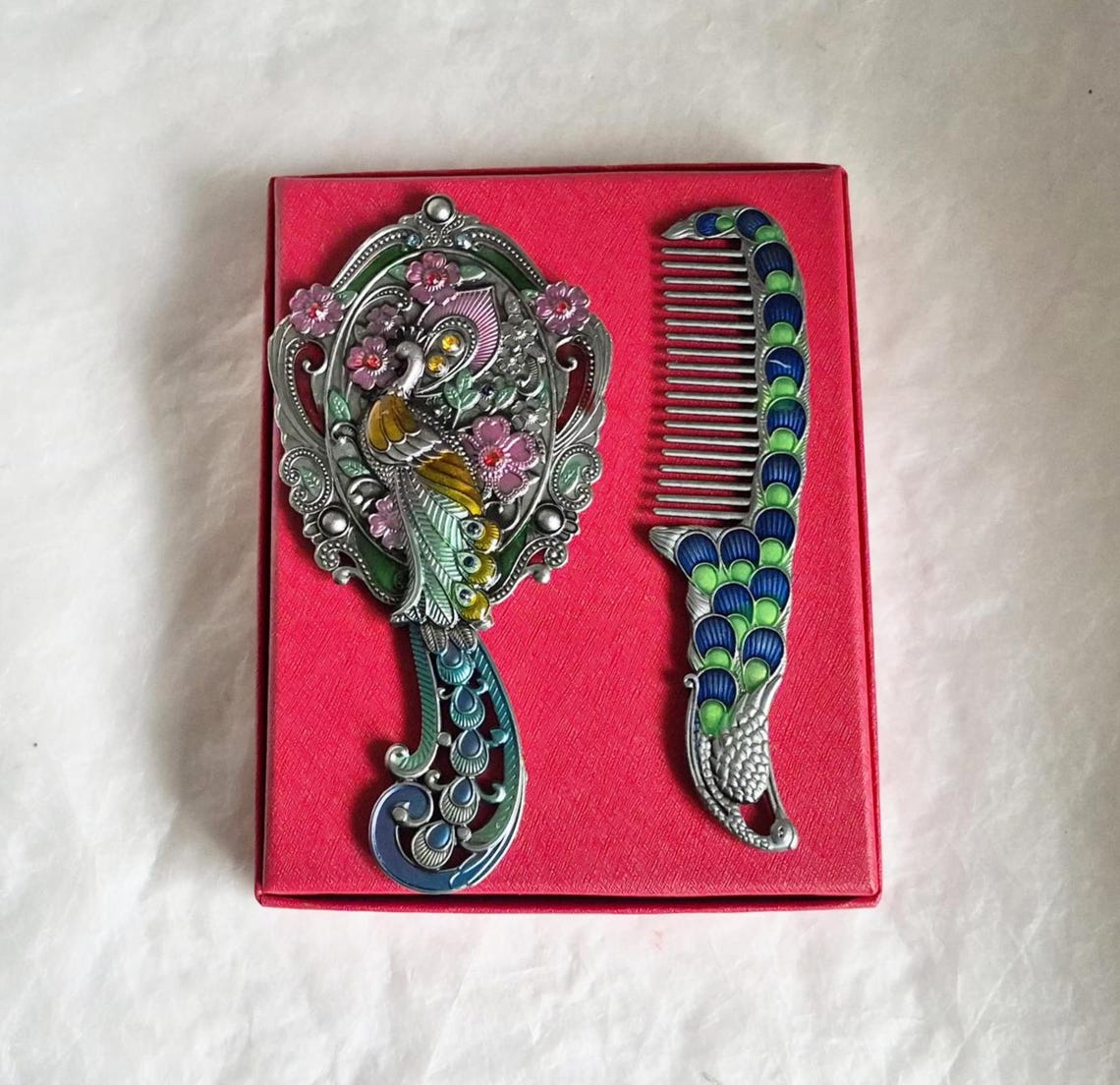 Top view of mirror and comb from boxed vintage style enamelled hand mirror and comb, intricate teal, pink and silver peacock diamanté patterned fascia.