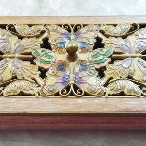 Peut inclure: Une boîte rectangulaire en bois avec un motif de papillons sur le couvercle. Les papillons sont dans des tons de violet, vert et or, avec un petit bouton au centre. La boîte a une base brun-rouge et un cadre brun clair.