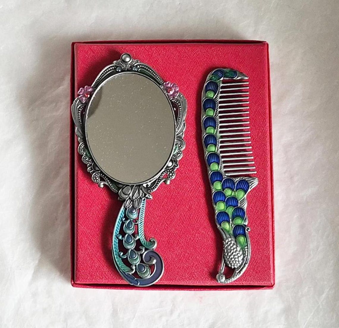 Underside of mirror and comb from boxed vintage style enamelled hand mirror and comb, intricate teal, pink and silver peacock diamanté patterned fascia.