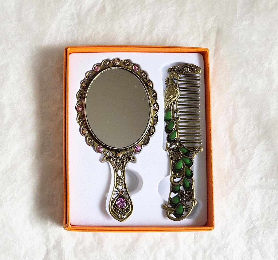 Underside of items inside box from vintage style enamelled hand mirror and comb, intricate green, pink and brass Peacock diamanté patterned fascia.