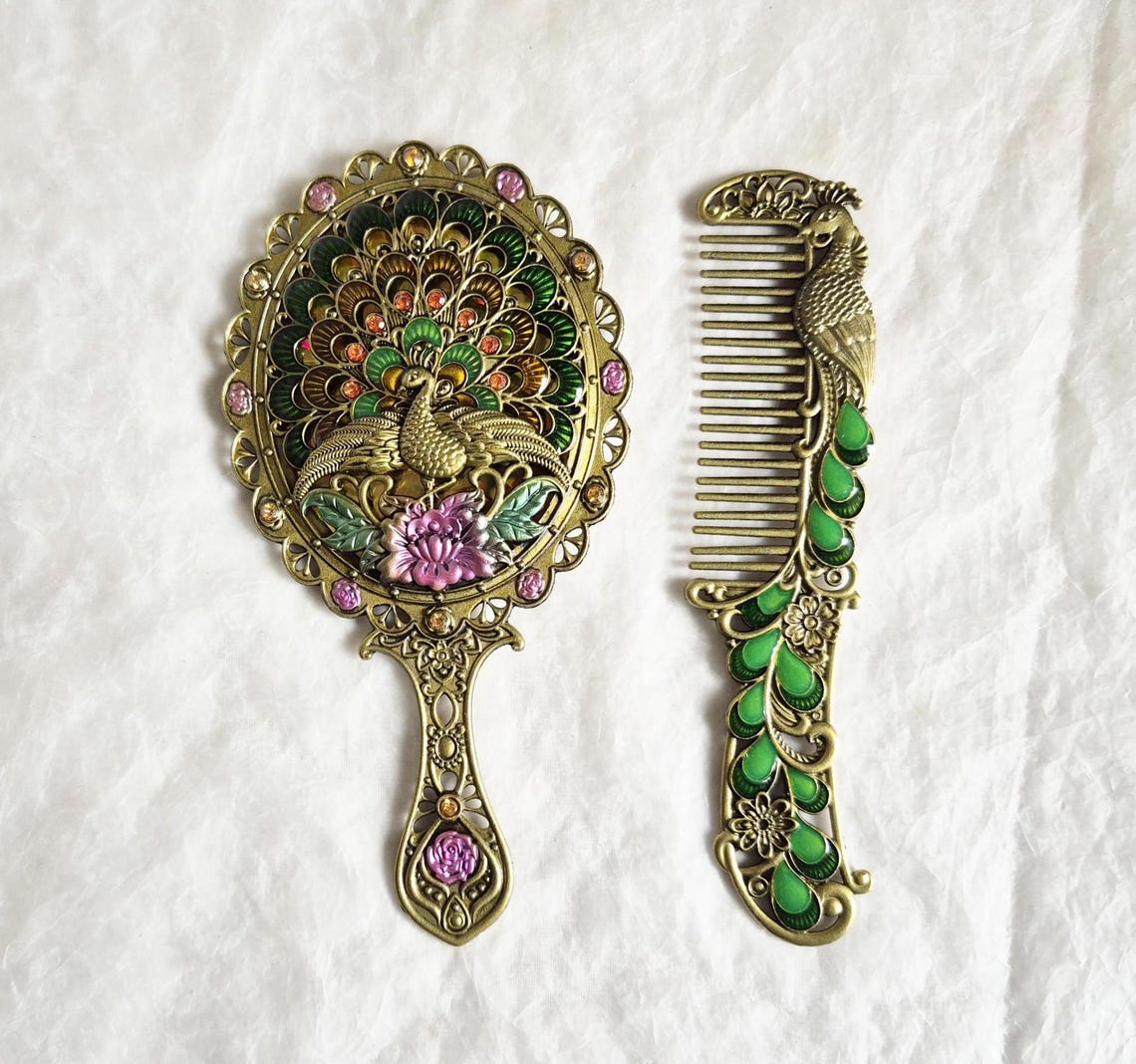 Top view of vintage style enamelled hand mirror and comb, intricate green, pink and brass Peacock diamanté patterned fascia.