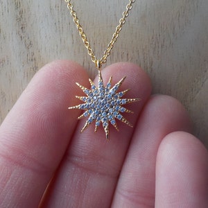 Puede incluir: Un collar de oro con un colgante de estrella en forma de estallido incrustado con diamantes de imitación transparentes.