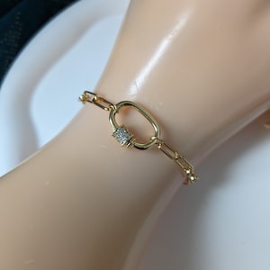 Peut inclure: Bracelet en chaîne dorée avec un grand fermoir ovale orné de pierres de zircone cubique transparentes.