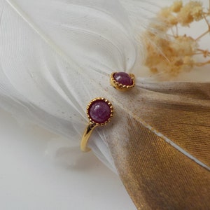Peut inclure: Une bague en or avec deux accents de pierres précieuses roses. La bague est ouverte et a un design délicat.