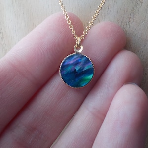 Peut inclure: Un collier en cha&icirc;ne dor&eacute;e avec un pendentif rond bleu et vert iridescent.