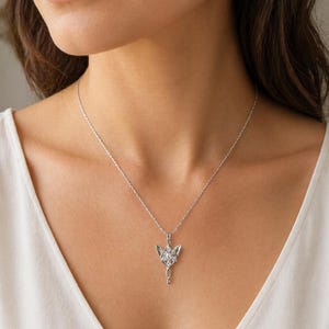 Puede incluir: Un collar con colgante plateado con un diseño de hoja estilizada y una piedra preciosa central transparente. El colgante cuelga de una cadena delicada, creando un accesorio elegante y llamativo.