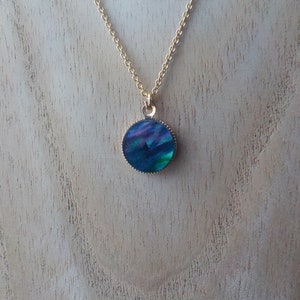 Peut inclure: Un collier en cha&icirc;ne dor&eacute;e avec un pendentif rond bleu iridescent.