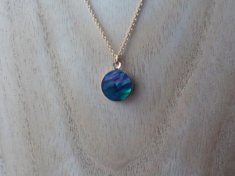 Peut inclure: Un collier en cha&icirc;ne dor&eacute;e avec un pendentif rond bleu iridescent.