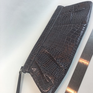 May include: A gray crocodile-embossed clutch purse with a long, thin strap.