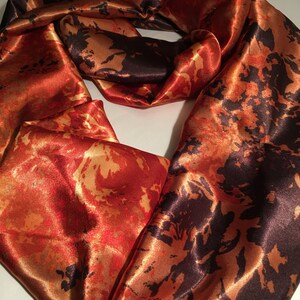 May include: A long, flowing scarf made of satin with a colorful abstract print in shades of orange, red, and black.