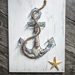May include: A blue and white anchor made of string wrapped around nails on a white wooden background. A starfish is in the bottom right corner.