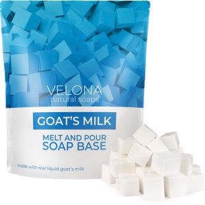 May include: A white bag of goat's milk melt and pour soap base. The bag has a blue design with the words "VELONA natural soaps" and "GOAT'S MILK MELT AND POUR SOAP BASE" printed on it. The bag is sitting on a white surface with a pile of white soap cubes in front of it.