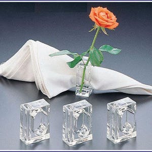 Pode incluir: Quatro argolas de guardanapo de acr&iacute;lico transparente com formato quadrado. As argolas s&atilde;o projetadas para segurar um guardanapo e um pequeno arranjo de flores. Uma &uacute;nica rosa laranja &eacute; exibida em um vaso de acr&iacute;lico transparente.