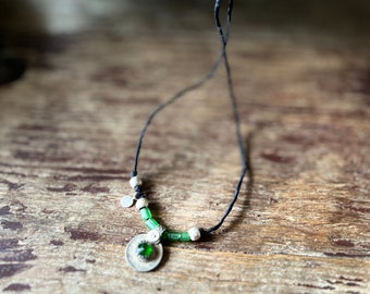 Black silk cord, its vintage green kucchi charm, can be worn as a necklace or tied around the wrist