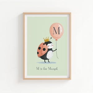 Puede incluir: Una impresión enmarcada con una mariquita de dibujos animados sosteniendo un globo con la letra "M". La mariquita lleva una corona y tiene un caparazón rojo y negro. El globo es de color melocotón y el fondo es verde claro. El texto "M is for Margot" está en la parte inferior.