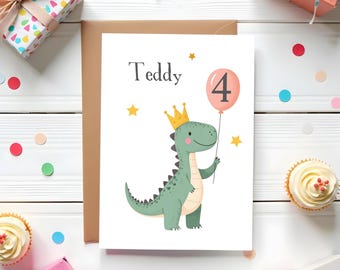 May include: A birthday card with a green dinosaur wearing a gold crown and holding a pink balloon with the number 4. The card says "Teddy" in gray text. The card is on a white wooden surface with gifts and confetti.