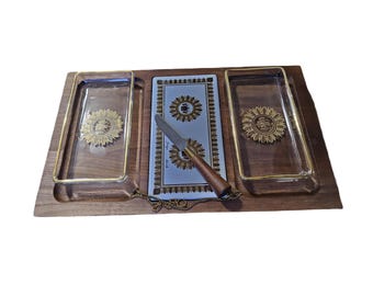 May include: A vintage serving tray with a wooden base, featuring two clear glass rectangular dishes with gold trim and a central ceramic section. The ceramic section has a light blue background with gold sunflower designs. A cheese knife with a wooden handle rests on the tray.
