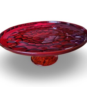 May include: A vibrant red glass serving dish with a textured surface and a pedestal base. The dish has an oval shape and is likely used for displaying food or decorative items. The color is a deep, rich red.