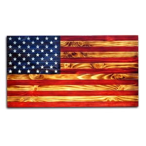 May include: A wooden American flag with red, white, and blue paint. The flag is made of individual wood planks, giving it a rustic look. The stars are white and the stripes are red and white.
