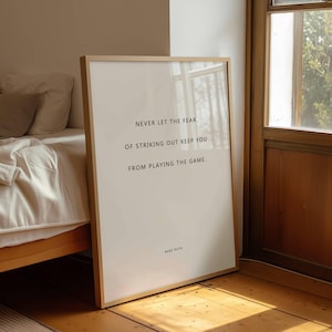 Pode incluir: Uma peça de arte de parede retangular emoldurada com uma moldura de madeira clara e fundo branco com texto preto que diz: NEVER LET THE FEAR OF STRIKING OUT KEEP YOU FROM PLAYING THE GAME. O nome BABE RUTH está impresso abaixo do texto.