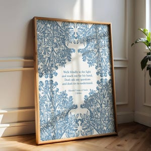 Puede incluir: Un estampado enmarcado con un diseño botánico azul y crema. La obra de arte presenta un patrón floral que rodea un texto central que dice: "Walk blindly to the light and reach out for his hand..." El marco es de madera.