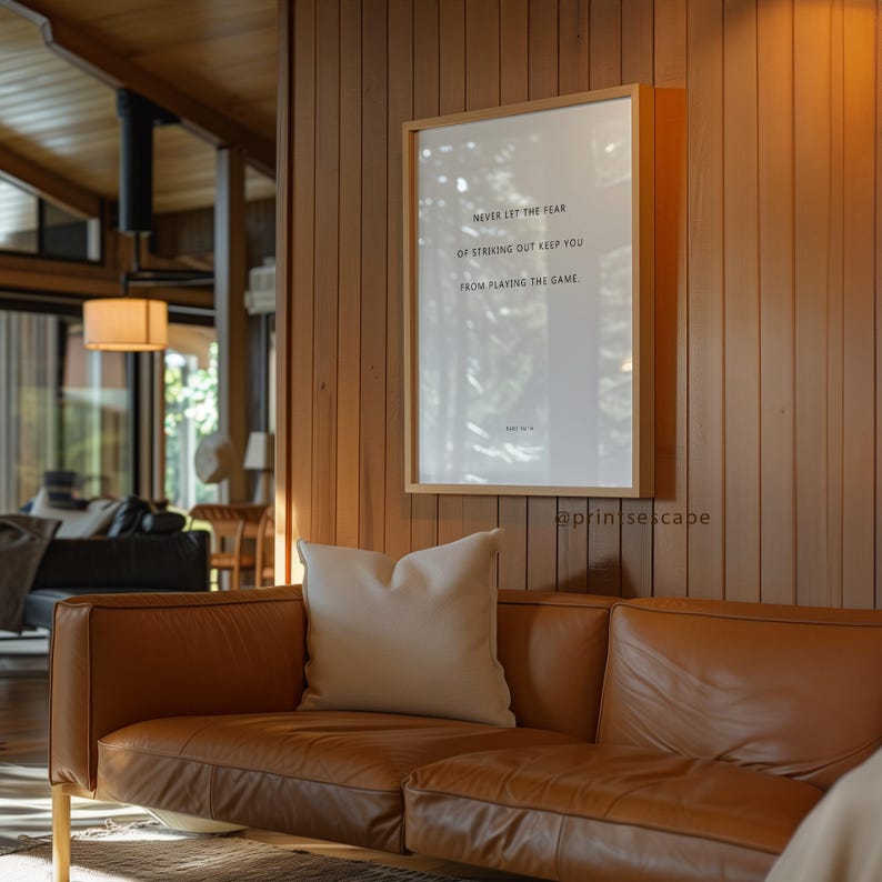Modern motivational art with Babe Ruth’s quote, displayed in a sleek living room on a wooden-paneled wall above a tan leather couch.