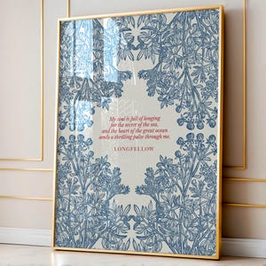 Puede incluir: Una impresión artística enmarcada con un marco dorado. La obra de arte presenta un diseño floral azul y blanco que rodea una cita de Longfellow. La cita dice: "Mi alma está llena de anhelo por el secreto del mar, y el corazón del gran océano envía un pulso emocionante a través de mí."