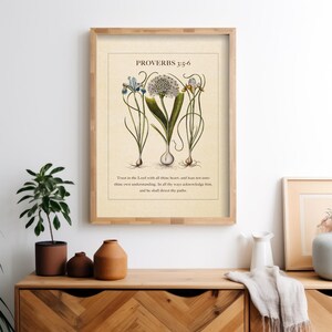 Printable featuring Proverbs 3:5-6 Bible Verse paired with illustrated vintage botanicals shown in a wood frame above a wooden sideboard with vases and a blanket.