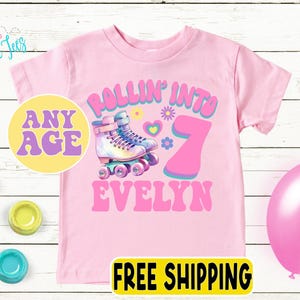 May include: A pink t-shirt featuring a roller skate design and the text "ROLLIN' INTO 7 EVELYN". The design includes a roller skate, flowers, and the words "ANY AGE". A pink balloon is on the right.