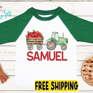 May include: White and green raglan-style shirt with a tractor and apple cart graphic. The name "SAMUEL" is printed in red. A pie and cinnamon sticks are also visible.