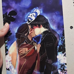 May include: An illustration of two figures embracing, set against a blue and purple background with floral accents. One figure wears a red and gold outfit, the other a black outfit. A blue and white mask sits atop one figure's head.