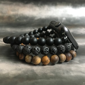 May include: Three beaded bracelets stacked on top of each other. The top bracelet is black, the middle bracelet is black and gray, and the bottom bracelet is brown.