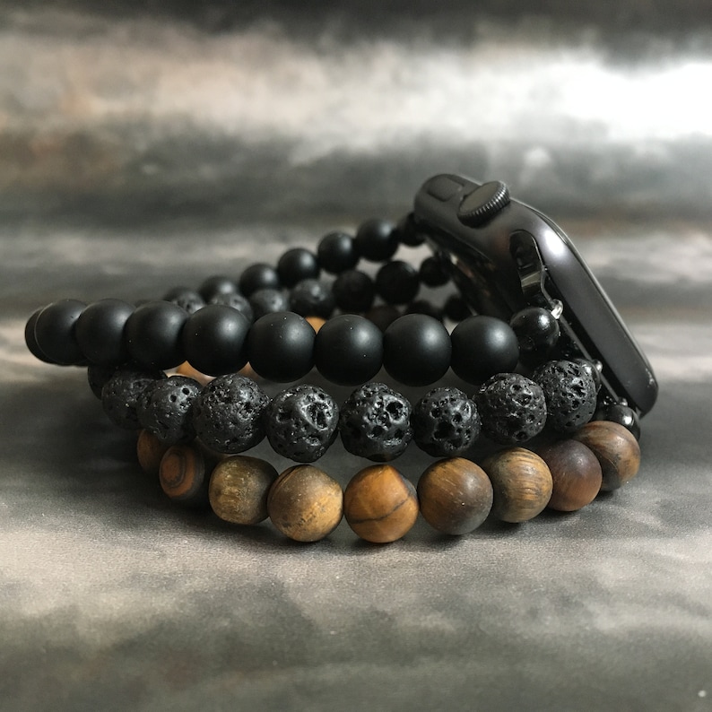 May include: Three beaded bracelets stacked on top of each other. The top bracelet is black, the middle bracelet is black and gray, and the bottom bracelet is brown.